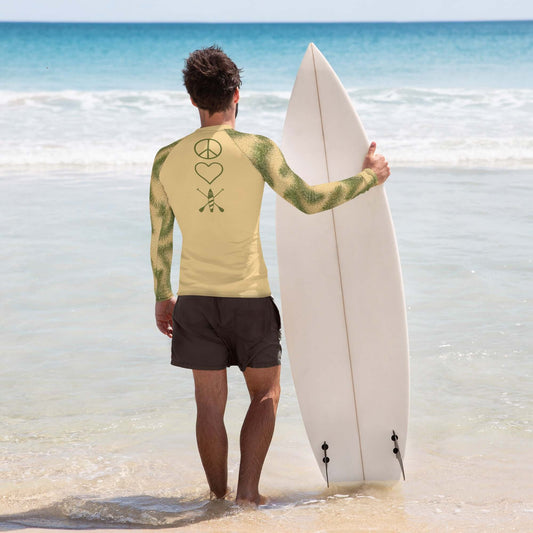 Man in Men's PNW BeachGrass Camo rash guard holding surfboard on sandy beach.