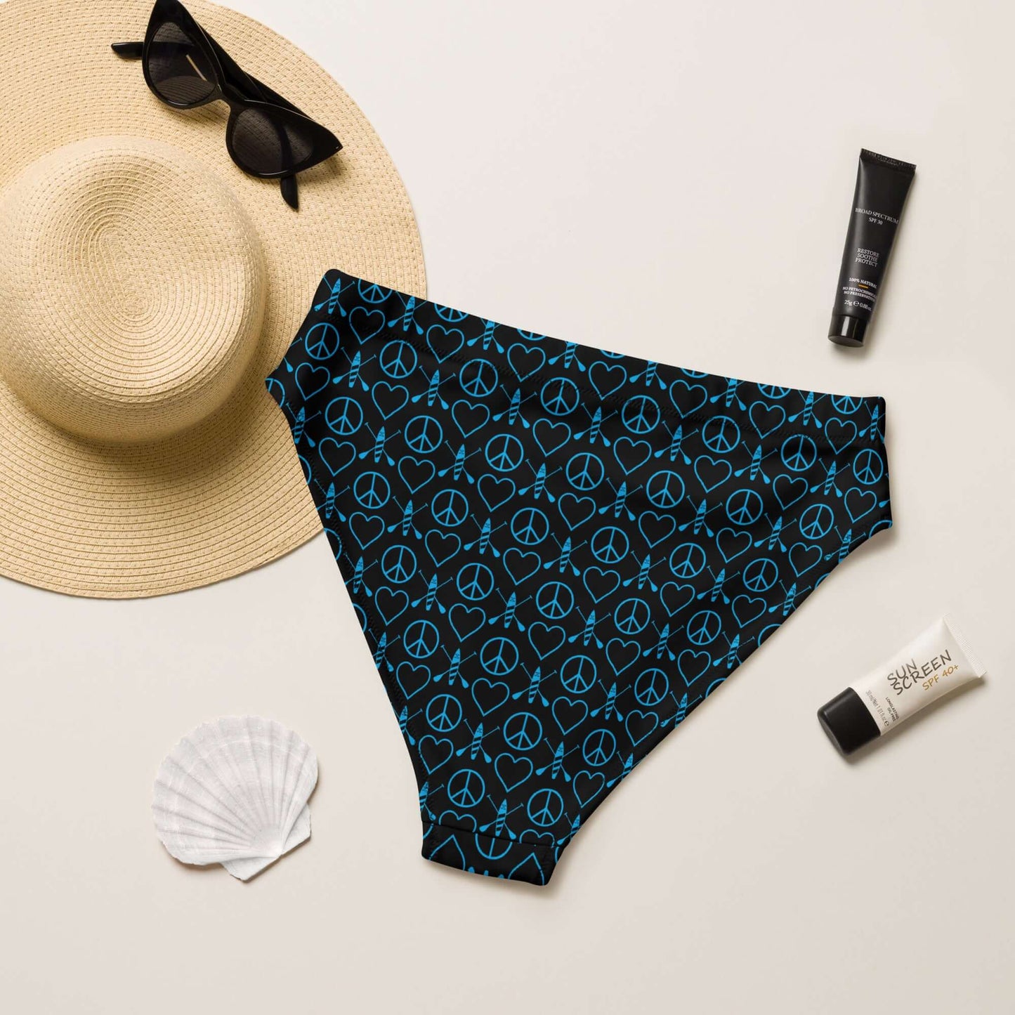 Recycled high-waisted bikini bottom in black with peace sign pattern, styled with beach accessories.