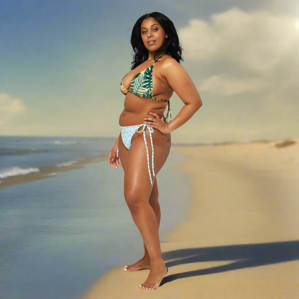 Model wearing a Recycled Peace Love Paddleboard string bikini on the beach, showcasing tropical print and stylish design.