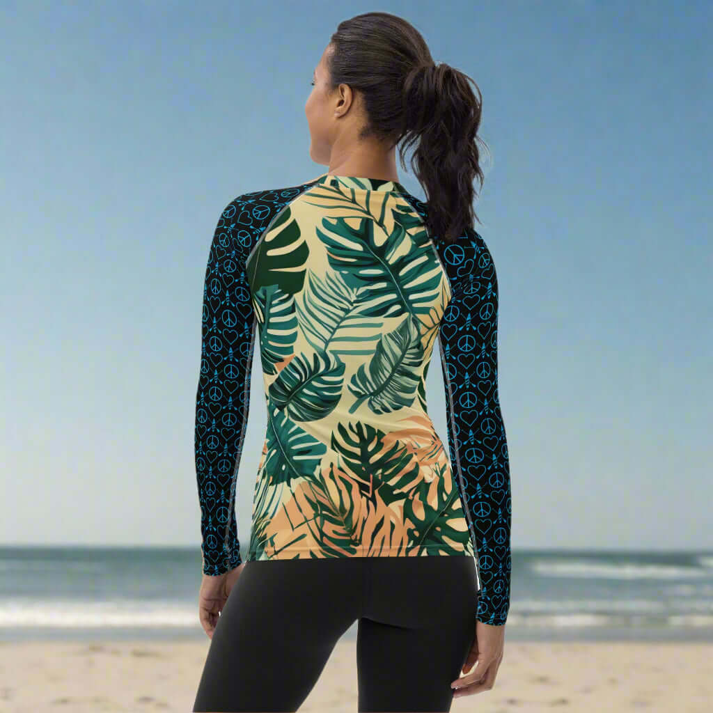 Woman wearing a stylish black rash guard with tropical print, perfect for beach sports.